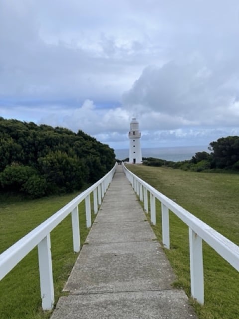 A picturesque pathway to a lighthouse on a grassy field along the Great Ocean Road.