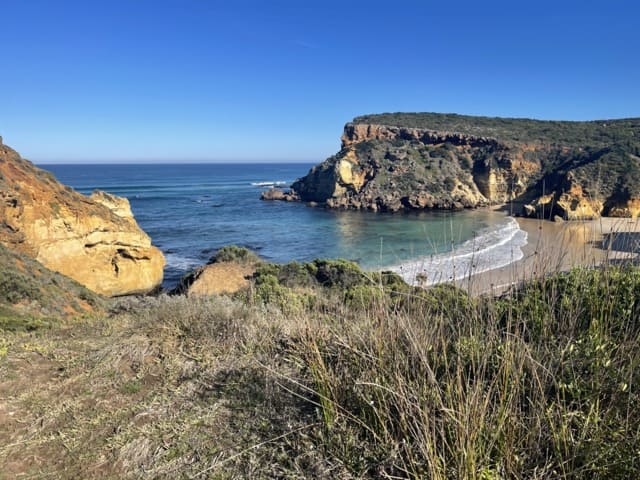 A scenic view of a beach and cliffs on the Great Ocean Road with a blue sky.