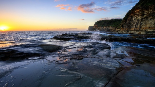 The sun is setting over a rocky cliff in sydney, new south wales.