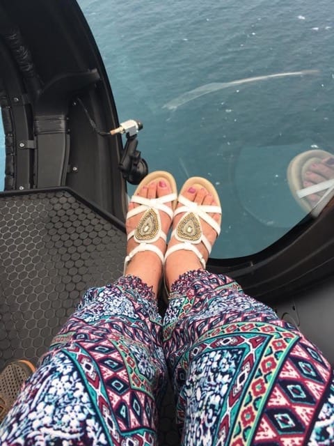 A person's feet in sandals hanging off the side of a helicopter on the Great Ocean Road.