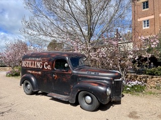 An old truck parked in front of a brick building near canola fields.