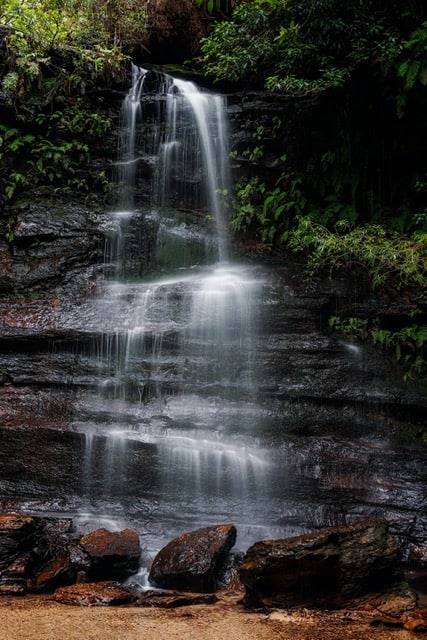 A picturesque waterfall in the middle of a wooded area, perfect for photography.