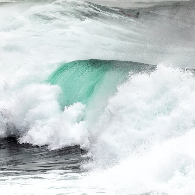 A surfer is riding a wave in the ocean, captured in seascape photography.