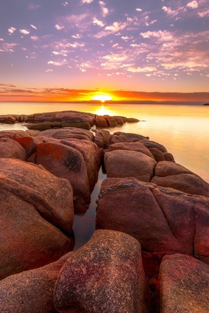 Editing landscape photos of the sun setting over rocks in the water.