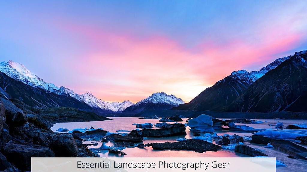 The image displays a majestic mountain range with snow-capped peaks under a gradient twilight sky of pink and blue. In the foreground, chunks of ice float in a tranquil glacial lake. A banner at the bottom reads "Essential Landscape Photography Gear." Location of background image: Tasman Lake, New Zealand