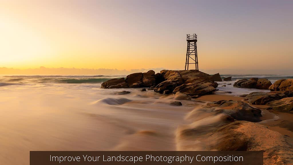 A serene beachscape at twilight with the soft glow of the sunrise or sunset illuminating the scene. A metal lifeguard tower stands atop a rock formation, surrounded by smooth, water-washed stones. The silky appearance of the ocean suggests a long exposure photograph, enhancing the tranquil mood of the scene. The caption "Improve Your Landscape Photography Composition" indicates the image may be used for educational purposes in photography composition techniques.