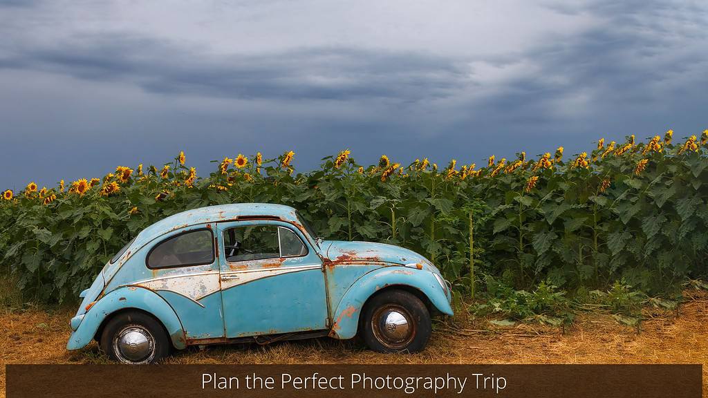 A weathered, light blue vintage Volkswagen Beetle parked on a dirt path adjacent to a vibrant field of sunflowers under a stormy sky, with the phrase "Plan the Perfect Photography Trip" displayed in the foreground.